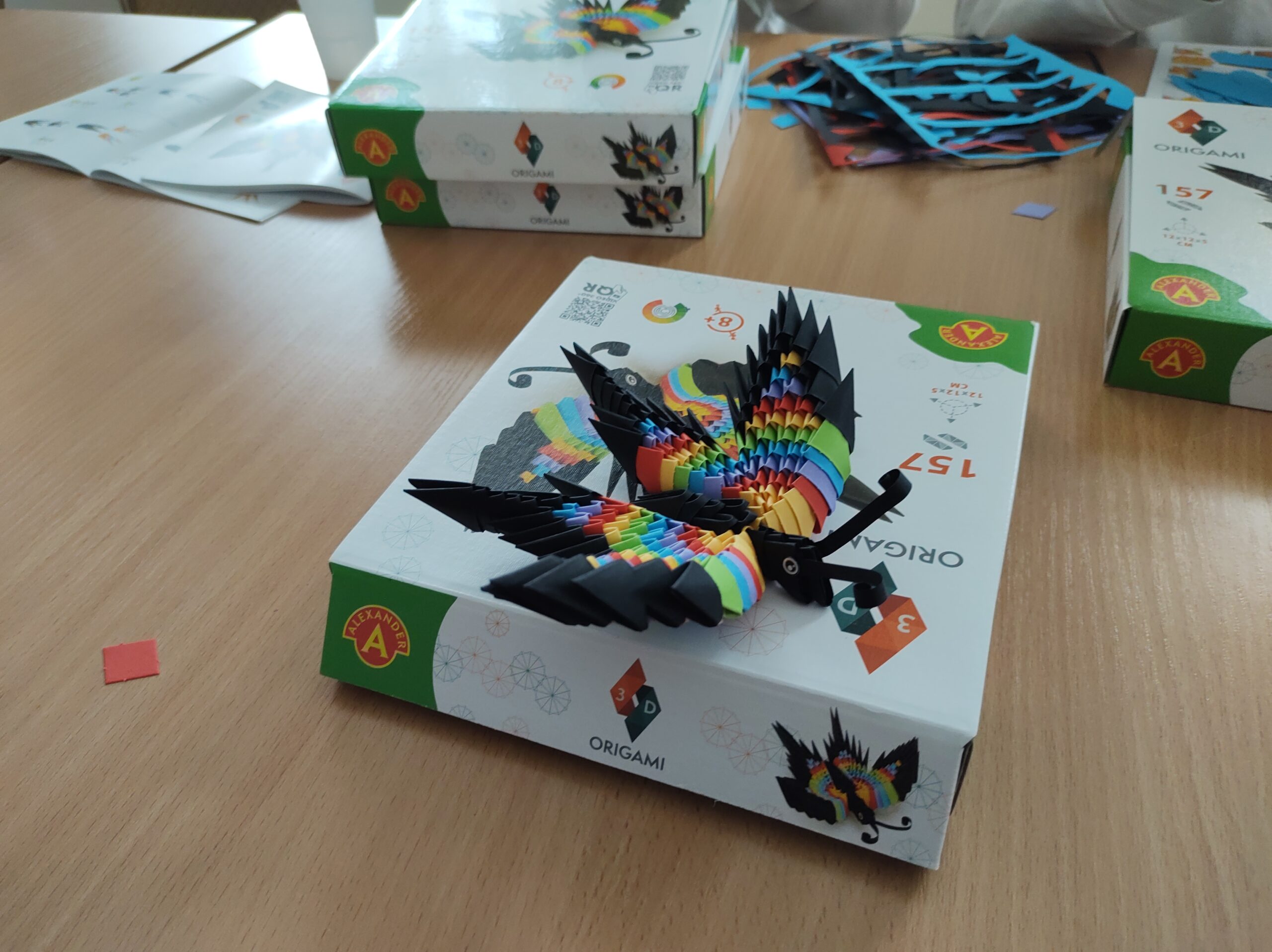 Na kartonowym pudełku leży motyl origami 3D