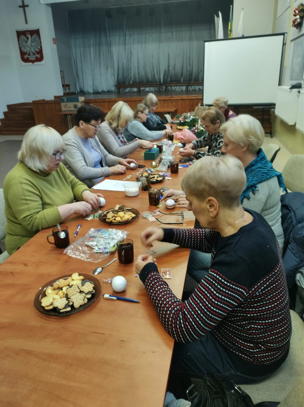 Przy stole siedzą kobiety i tworzą bombki.