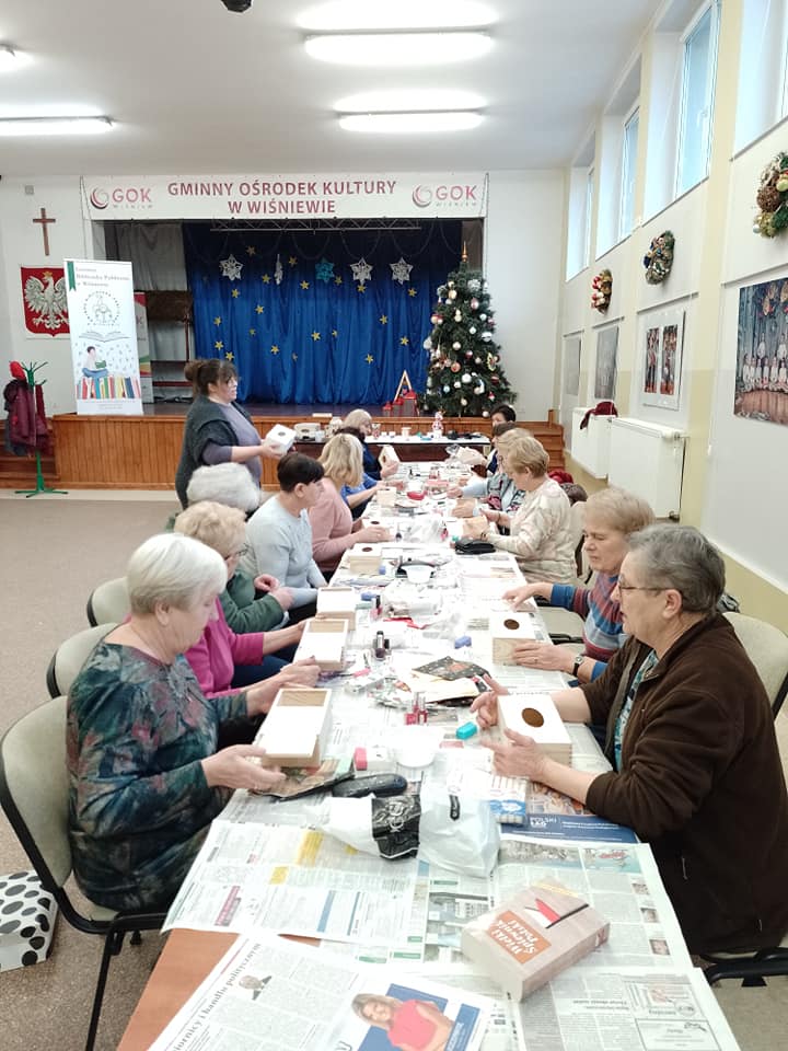 Wzdłuż długich stołów siedzą kobiety i wyklejają chusteczniki.